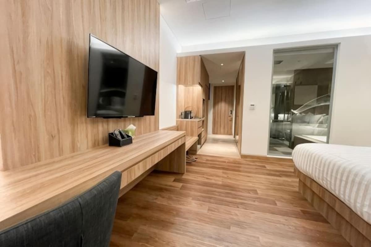 A modern hotel room with a flat-screen TV, wooden flooring, a desk, and a bed.