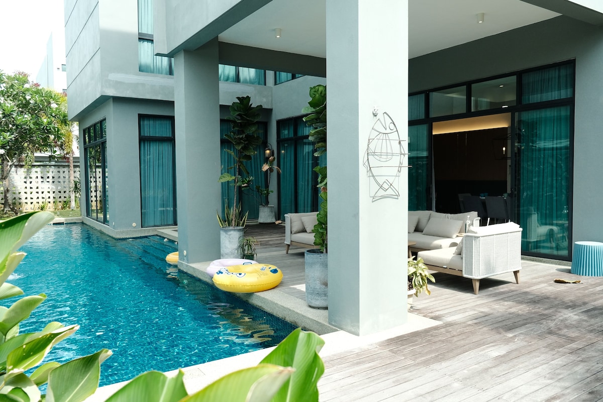 A modern outdoor pool area with a wooden deck, lounge chairs, and a yellow inflatable float.