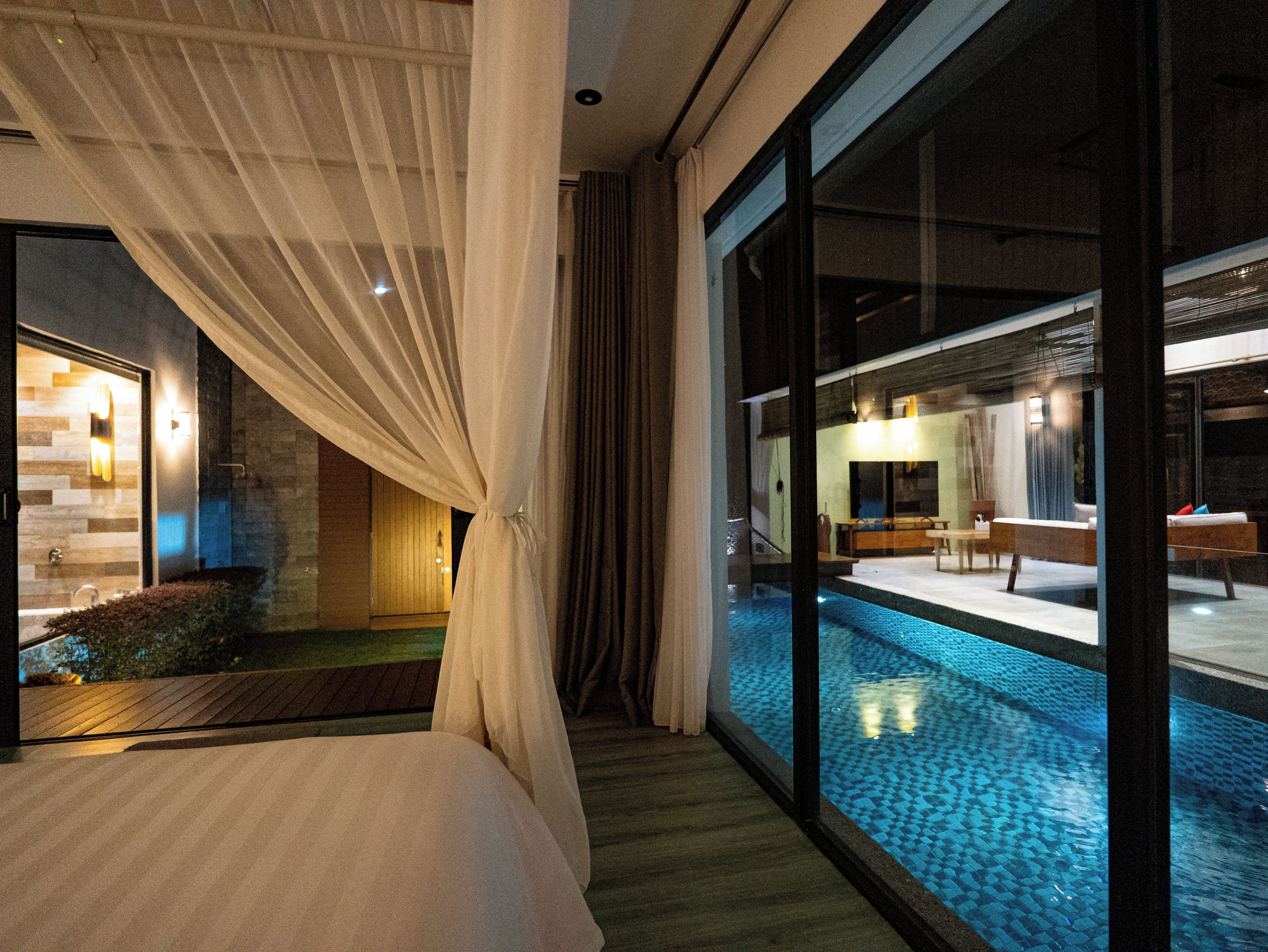 A bedroom with a large window, a bed, and a view of a pool area.