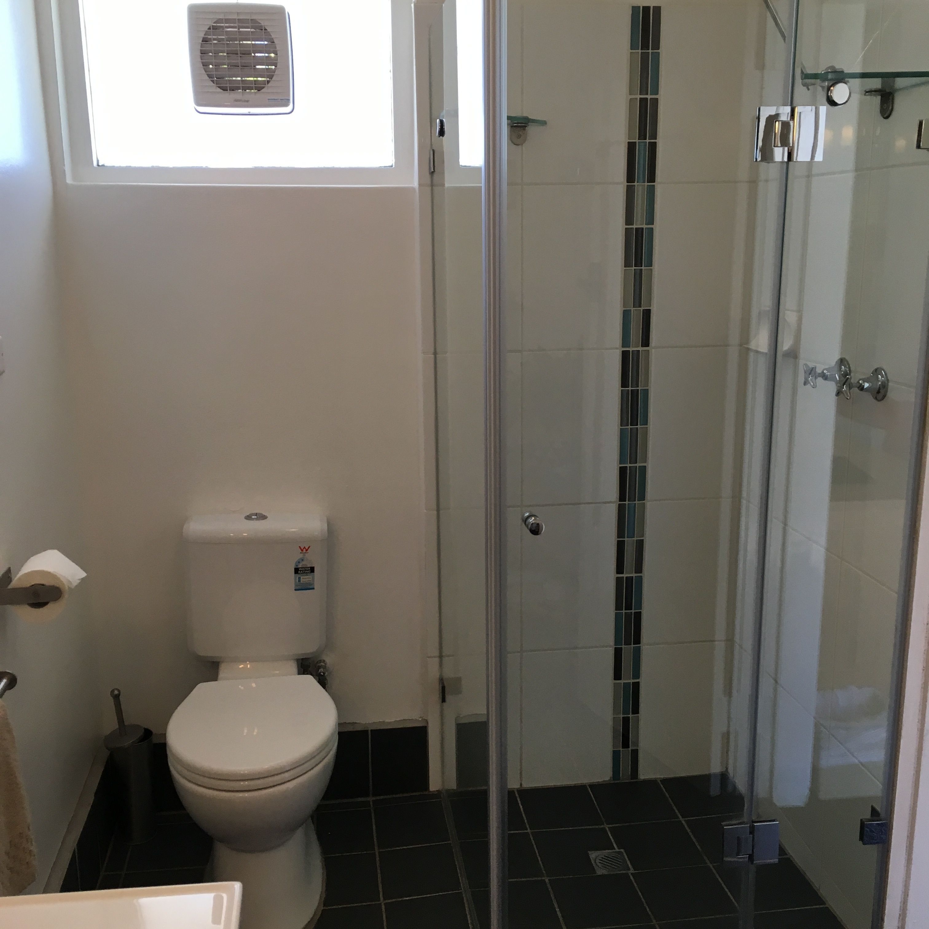 A bathroom with a toilet, a shower with a glass door, and a window above the toilet.