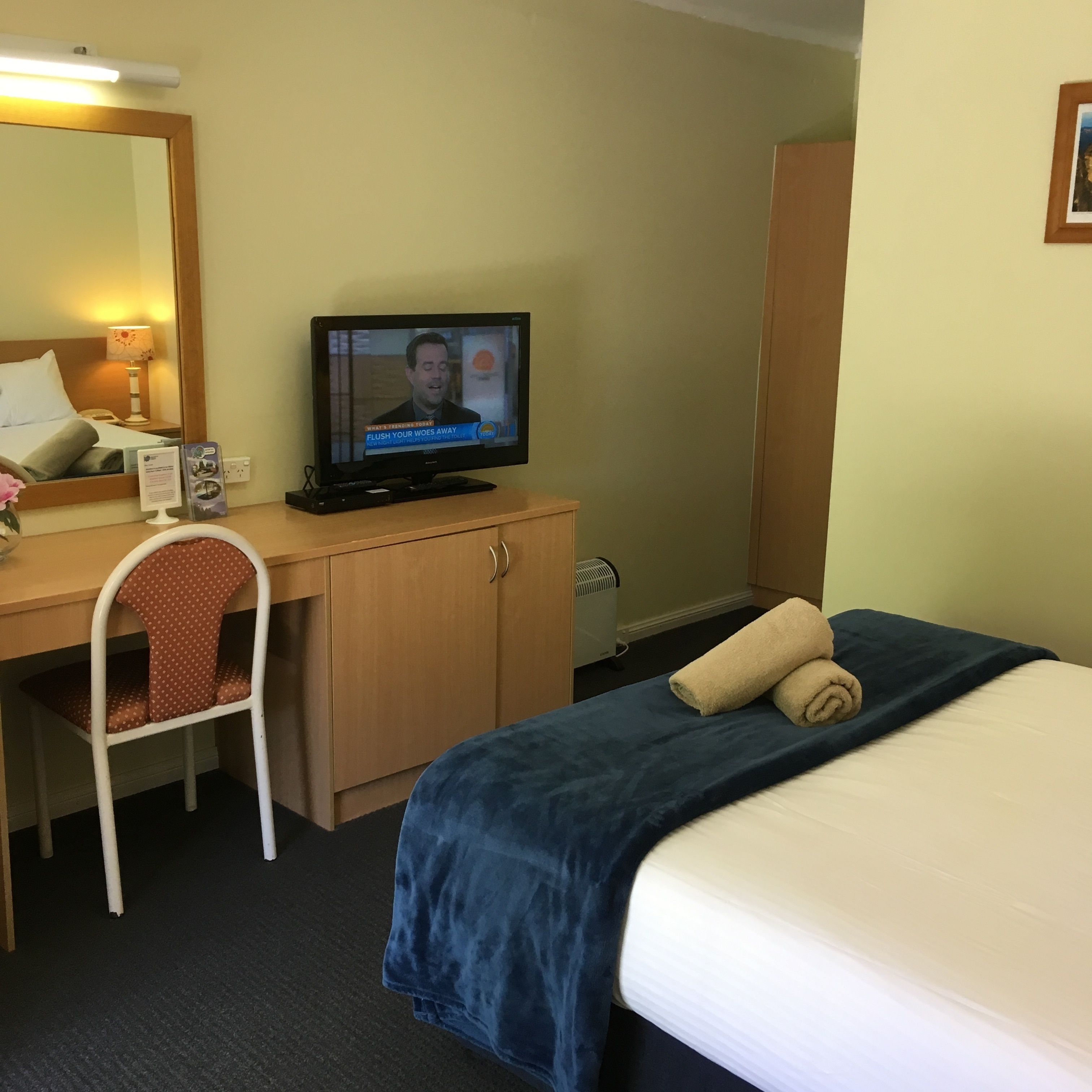 A hotel room with a bed, a desk with a television, a chair, and a wardrobe.
