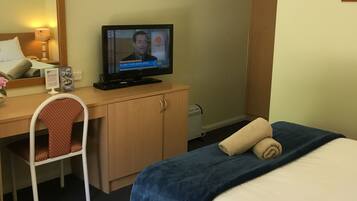 A hotel room with a bed, a desk with a television, a chair, and a wardrobe.