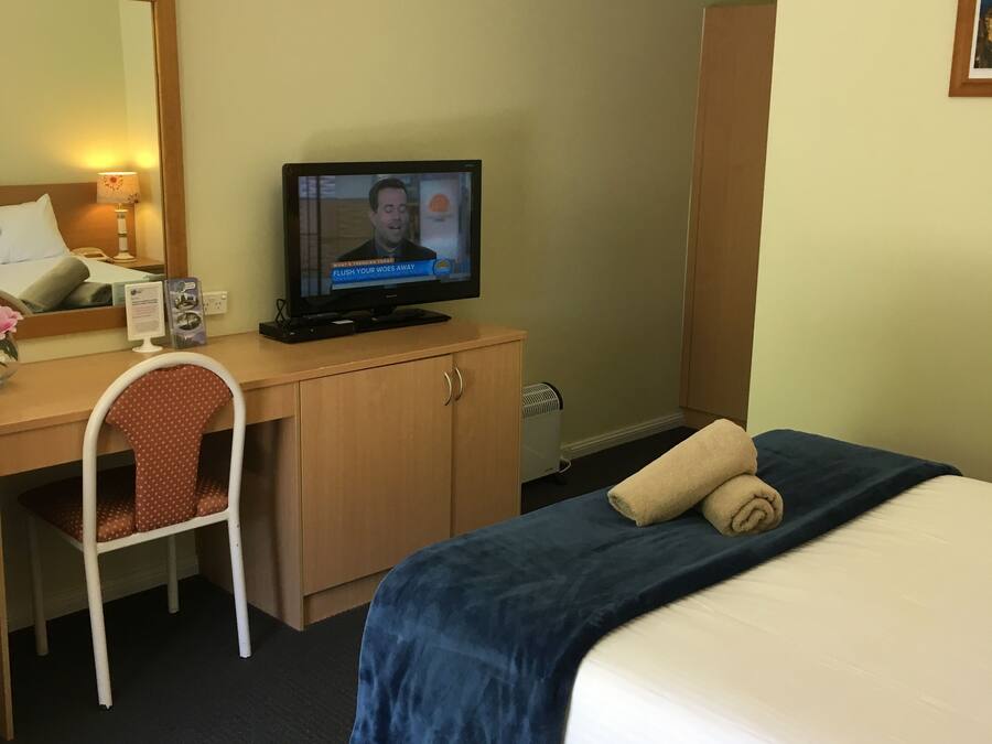 A hotel room with a bed, a desk with a television, a chair, and a wardrobe.