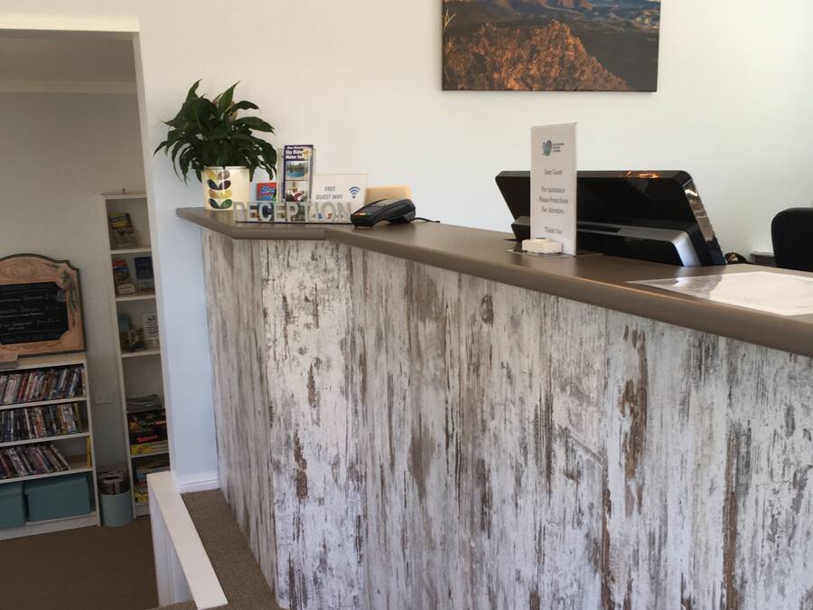 Un mostrador de recepción con detalles de madera rústica, un cuadro colgado con un paisaje, una planta y un cartel que indica WiFi gratuito para huéspedes.