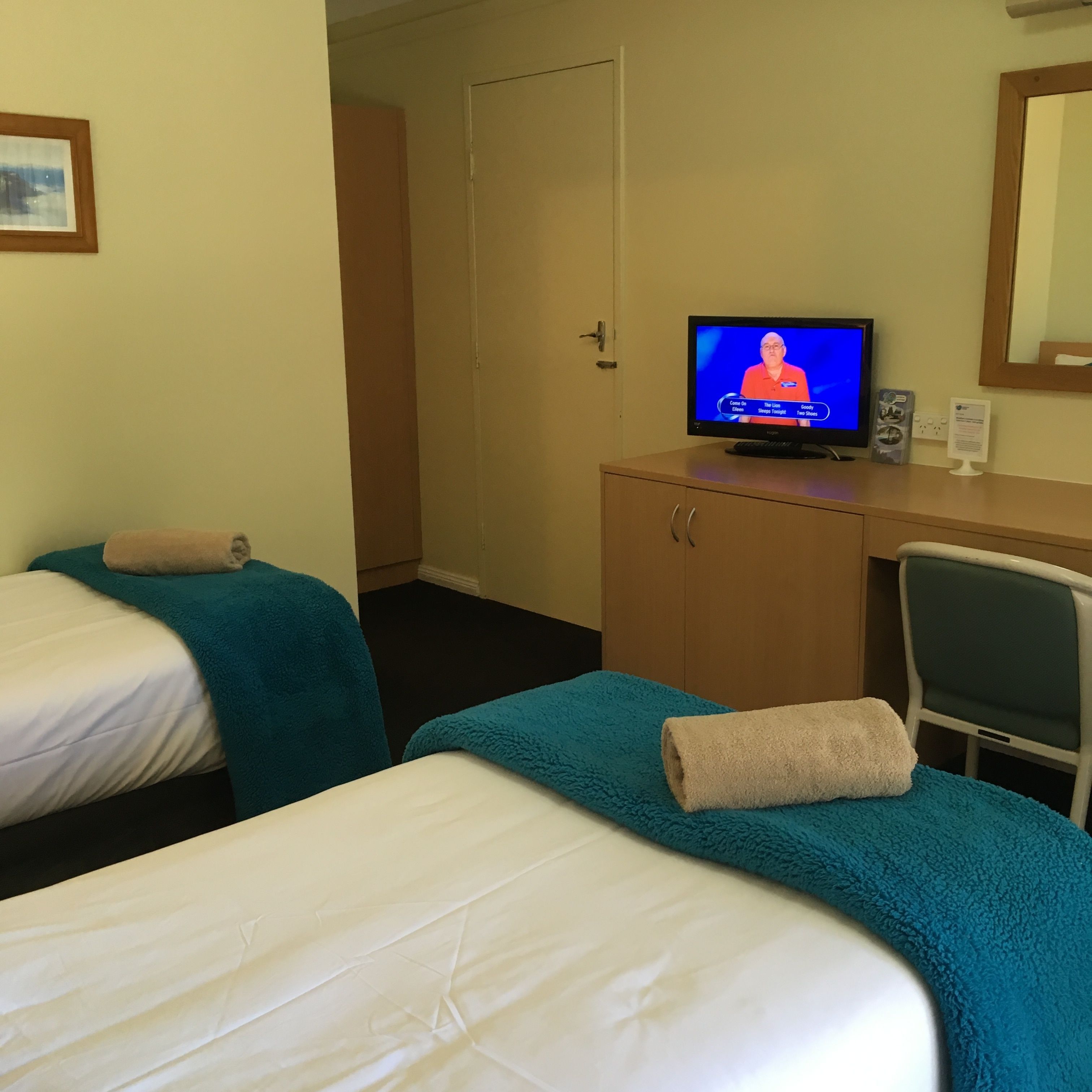 Una habitación de hotel con dos camas, un escritorio con televisor, una silla y una puerta.