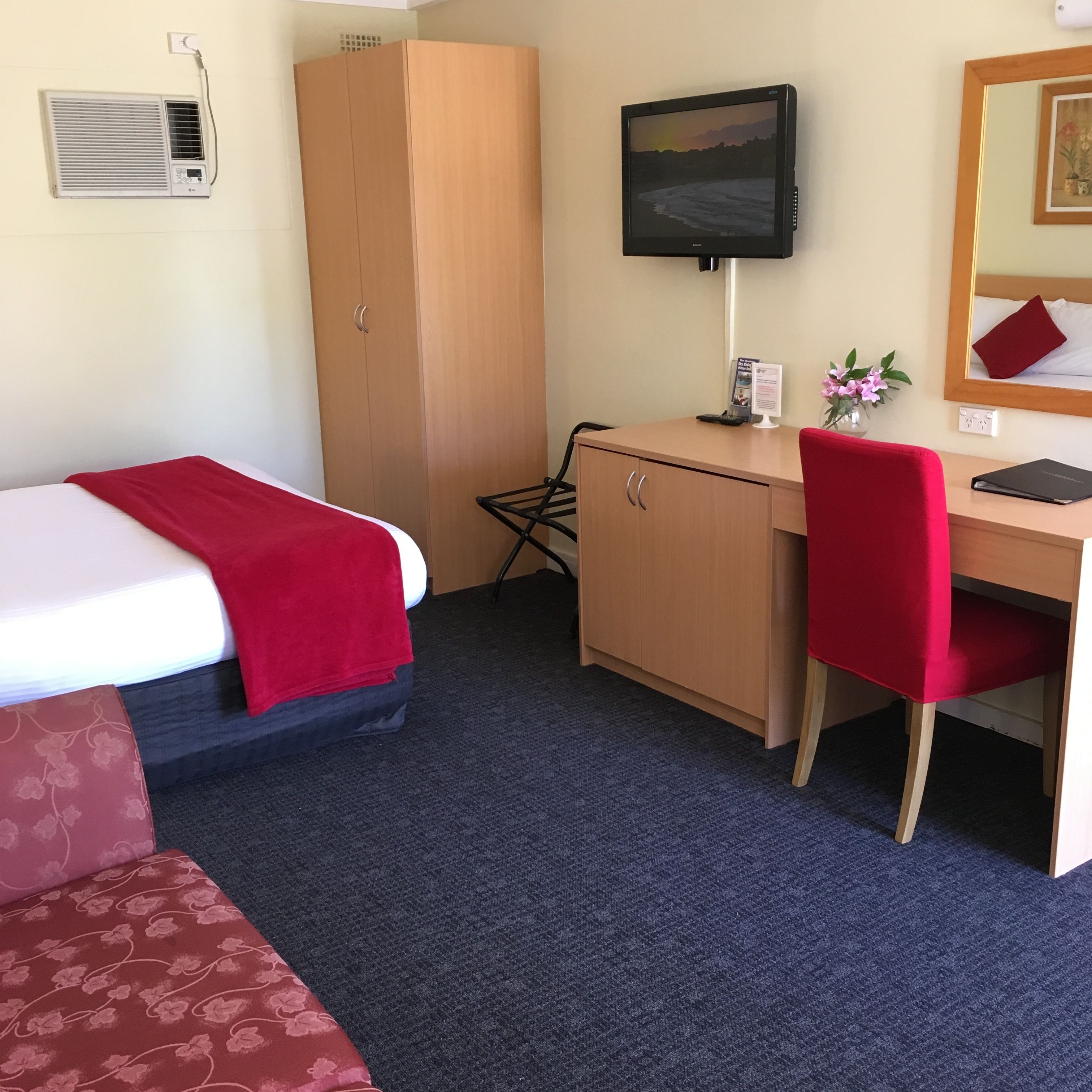 Ein Hotelzimmer mit Bett, Schreibtisch, Stuhl, Fernseher und Kleiderschrank.