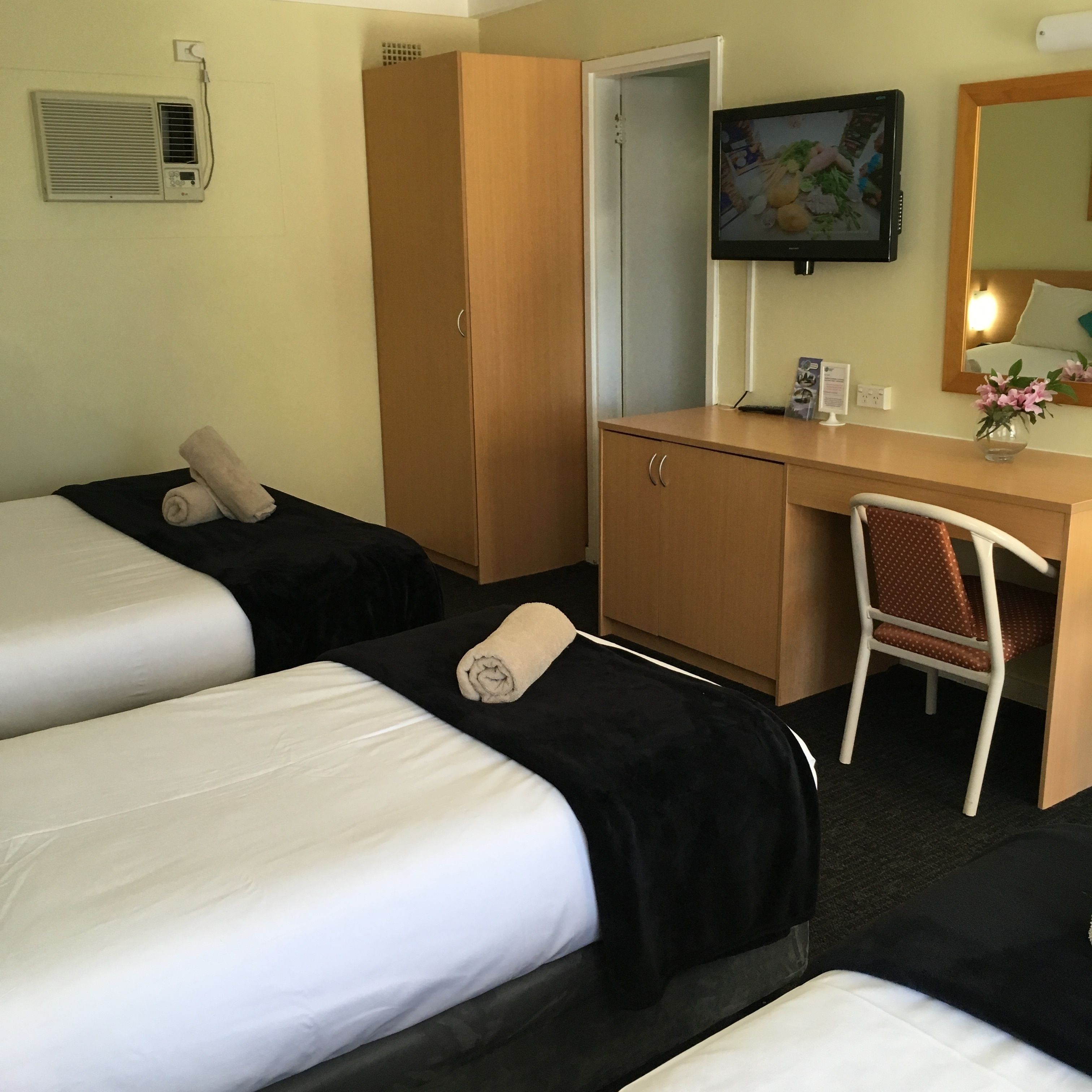 Quarto de hotel com duas camas, uma escrivaninha, uma cadeira, uma televisão e um guarda-roupa.