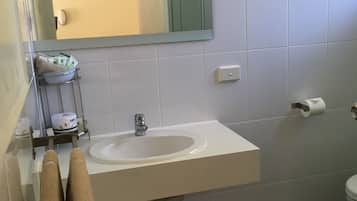 A bathroom with a white sink, a mirror, a towel rack, a toilet, and a trash bin.