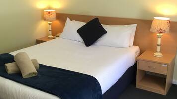 A neatly made bed with white linens, a dark blue bedspread, and a beige towel. There are two bedside tables with lamps, one of which has a label reading "Hair Dryer".