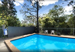 A rectangular swimming pool with a tiled edge, surrounded by a fence, and trees in the background. - Sky Rider Motor Inn (Katoomba)