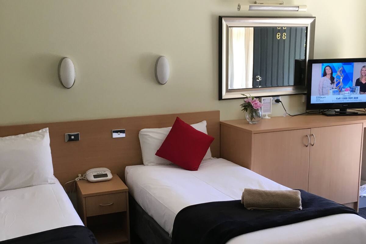 A hotel room with two beds, a TV, a mirror, and a small desk with a phone.