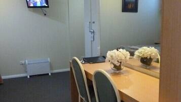 A small, private room with a single table, two chairs, a television mounted on the wall, a radiator, and a mirror reflecting the room.