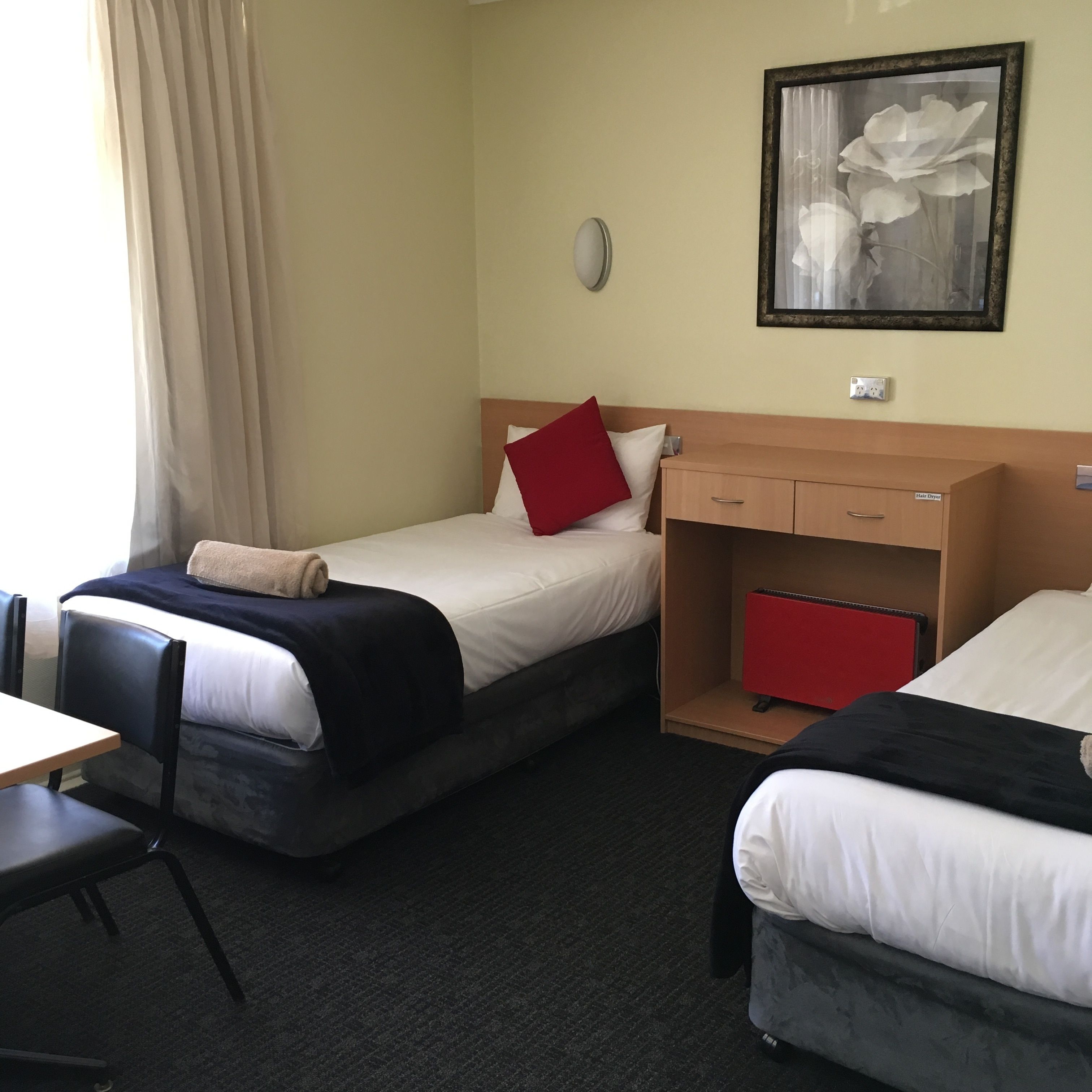 Une chambre d’hôtel avec deux lits, un bureau, une chaise, un sèche-cheveux et un tableau au mur.