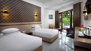 Quarto de hotel com duas camas, uma escrivaninha, uma cadeira, ar condicionado e vista para o verde lá fora.
