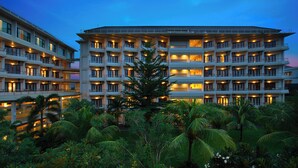 Um hotel com várias andares e varandas, rodeado por vegetação exuberante.