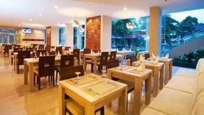 Um restaurante espaçoso com várias mesas e cadeiras, uma grande janela com vista para o exterior e uma televisão fixada na parede.