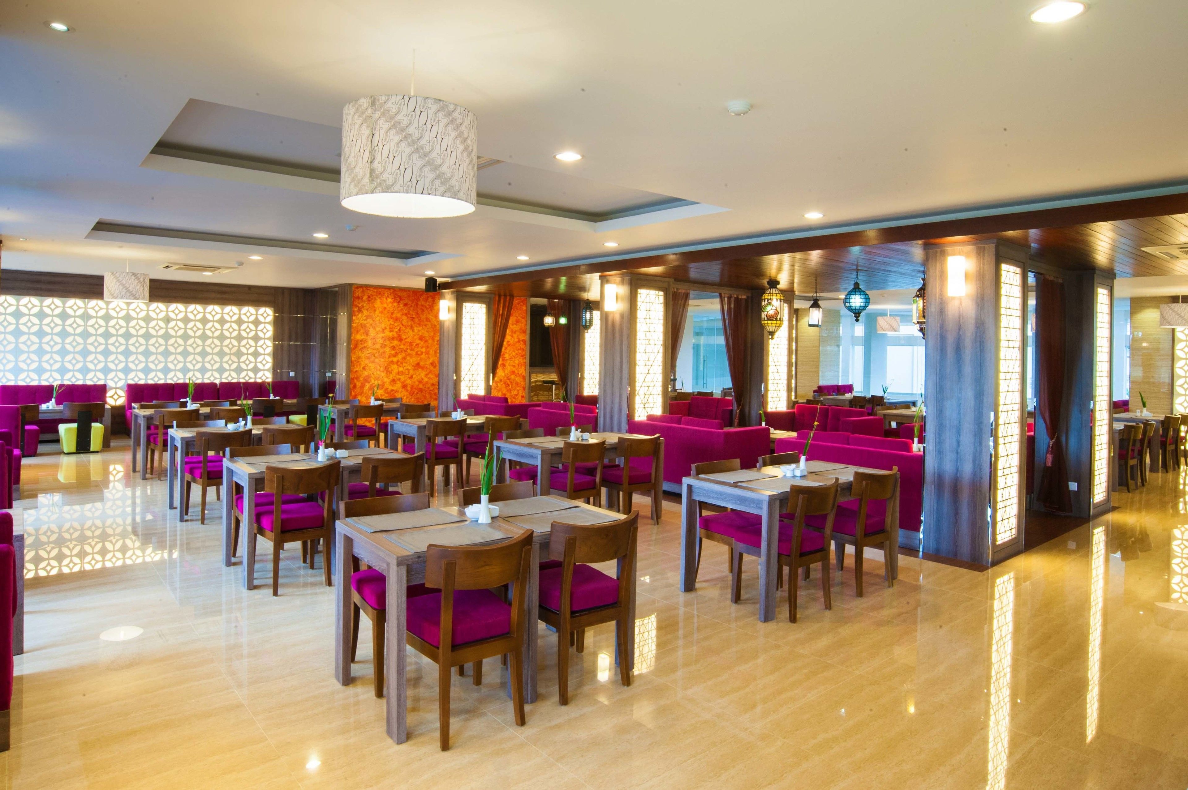 Un restaurante moderno con mesas y sillas de madera, decoración en tonos naranja brillante y púrpura, y un suelo pulido.