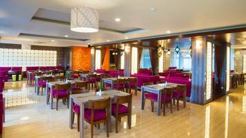 Un restaurante moderno con mesas y sillas de madera, decoración en tonos naranja brillante y púrpura, y un suelo pulido.