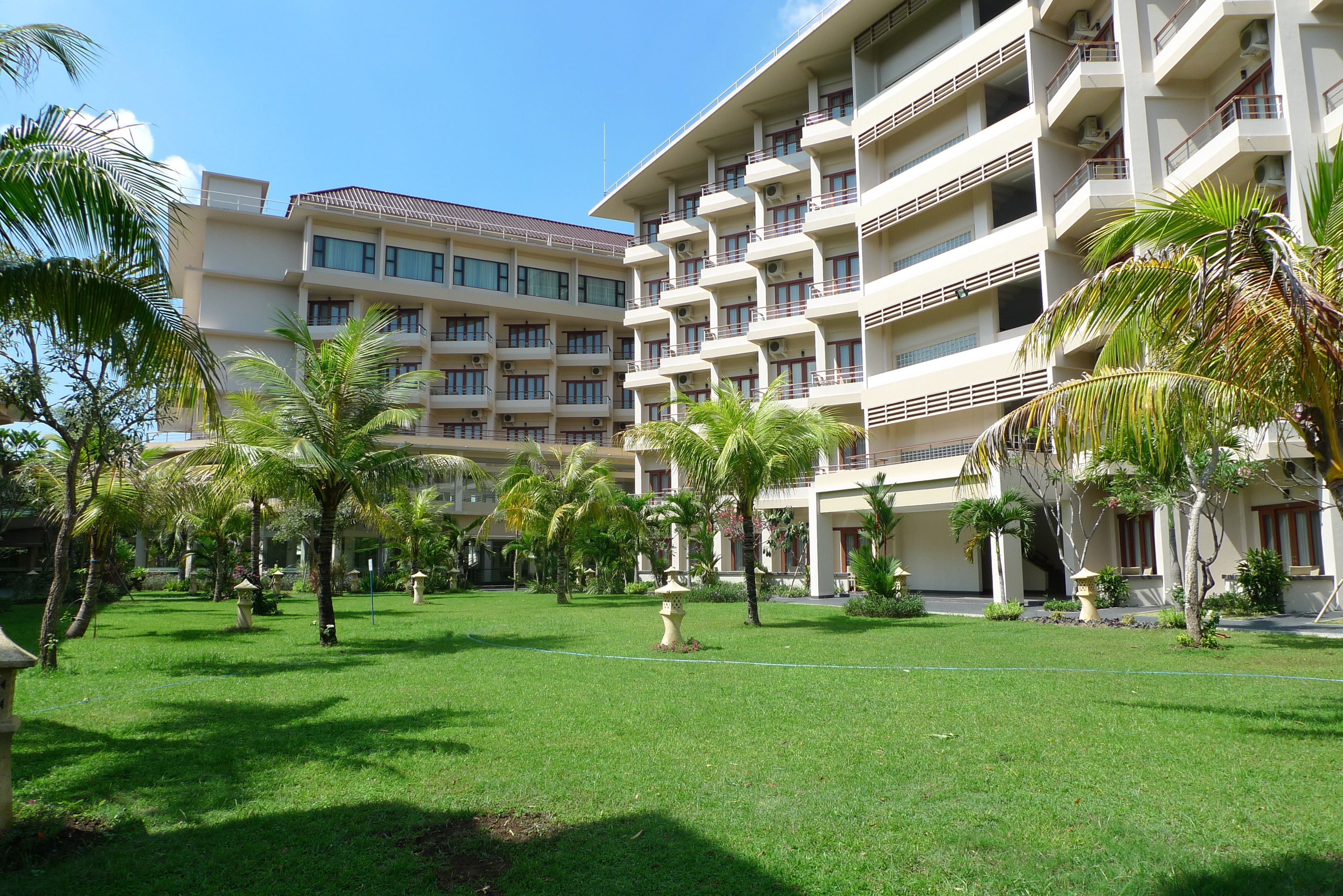 A multi-story hotel with a courtyard featuring palm trees and a well-maintained lawn.