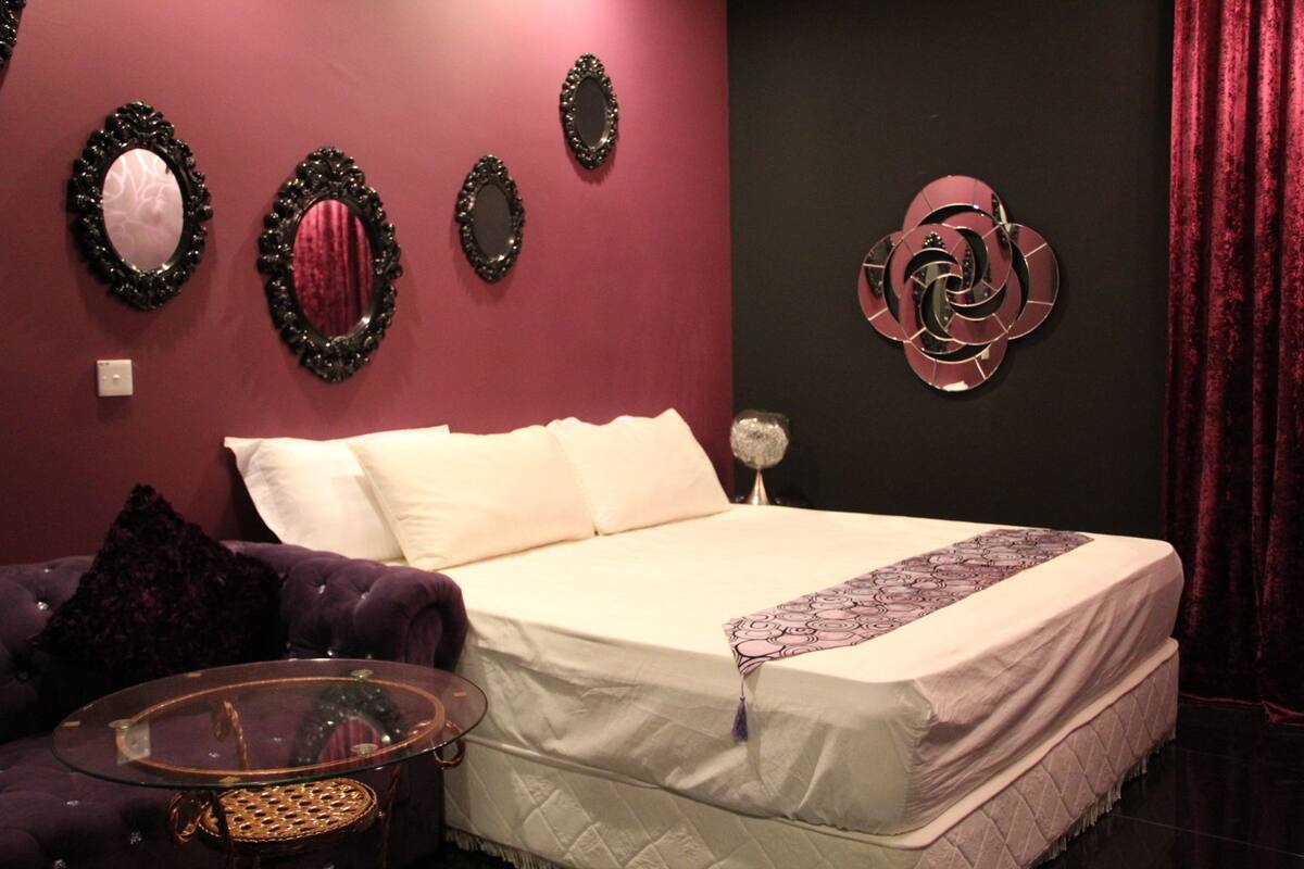 A bedroom with a bed, a glass coffee table, and decorative mirrors on the wall.
