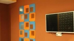Quarto com televisão na parede e painel decorativo com formas geométricas.