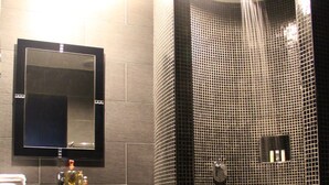 Uma casa de banho moderna com divisória de chuveiro em vidro, lavatório preto com espelho e uma toalha no chão.