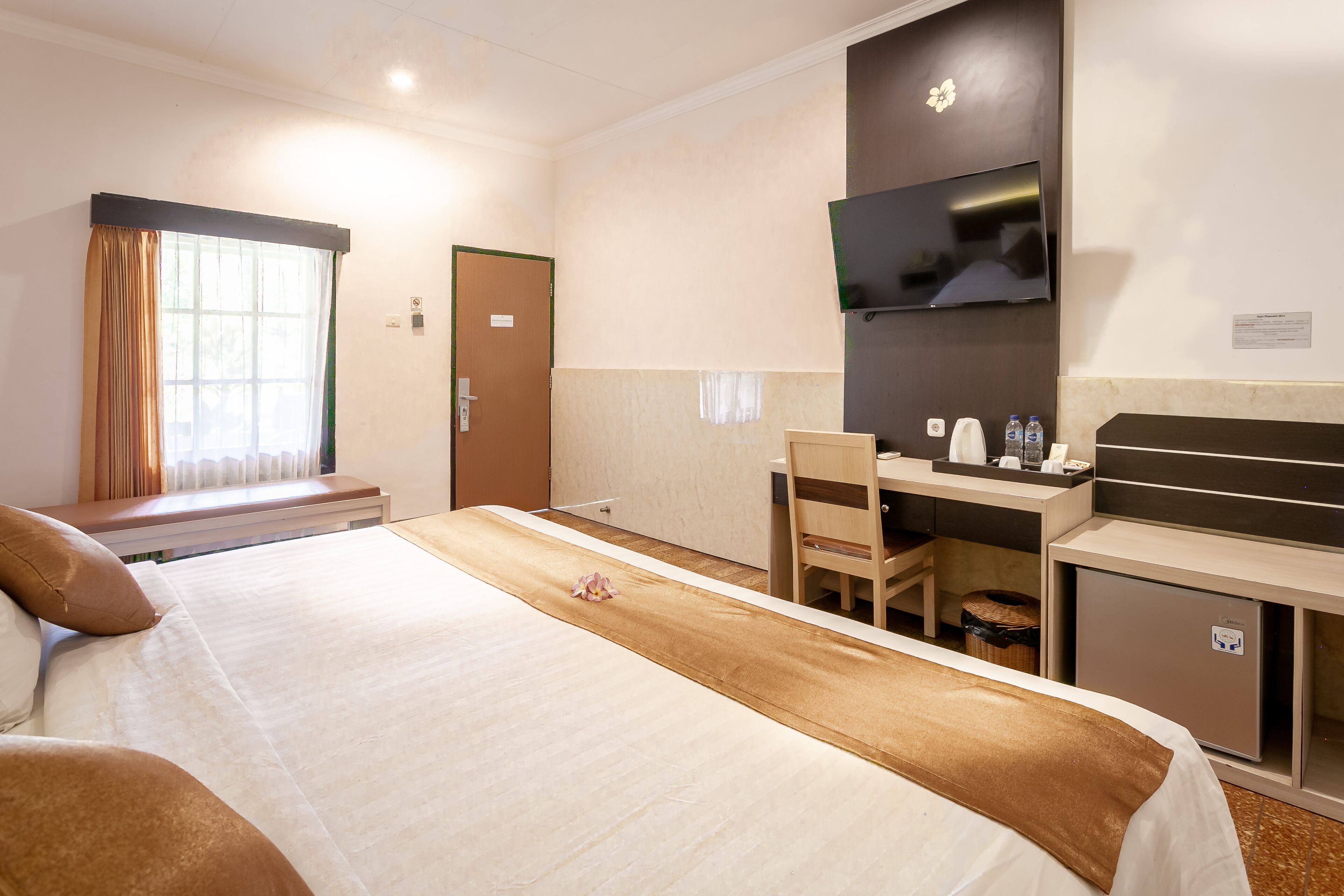 A hotel room with a bed, a desk, a chair, a TV, and a minibar.