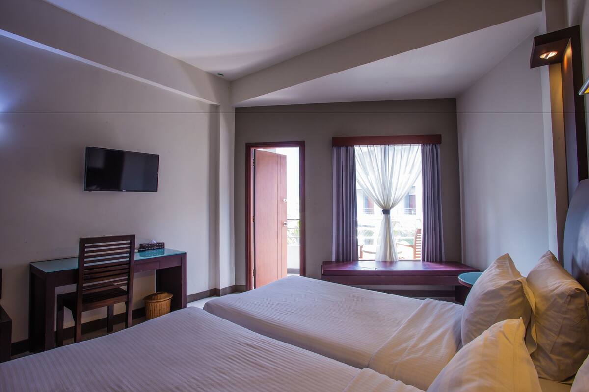 A hotel room with two beds, a desk, a chair, a TV, and a window with curtains.
