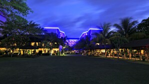 Un hotel grande con un patio central, rodeado de palmeras y una entrada bien iluminada.