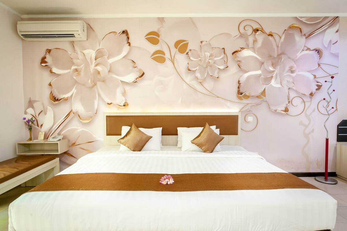 A hotel room with a large bed, a wooden headboard, and a decorative wall with floral patterns.