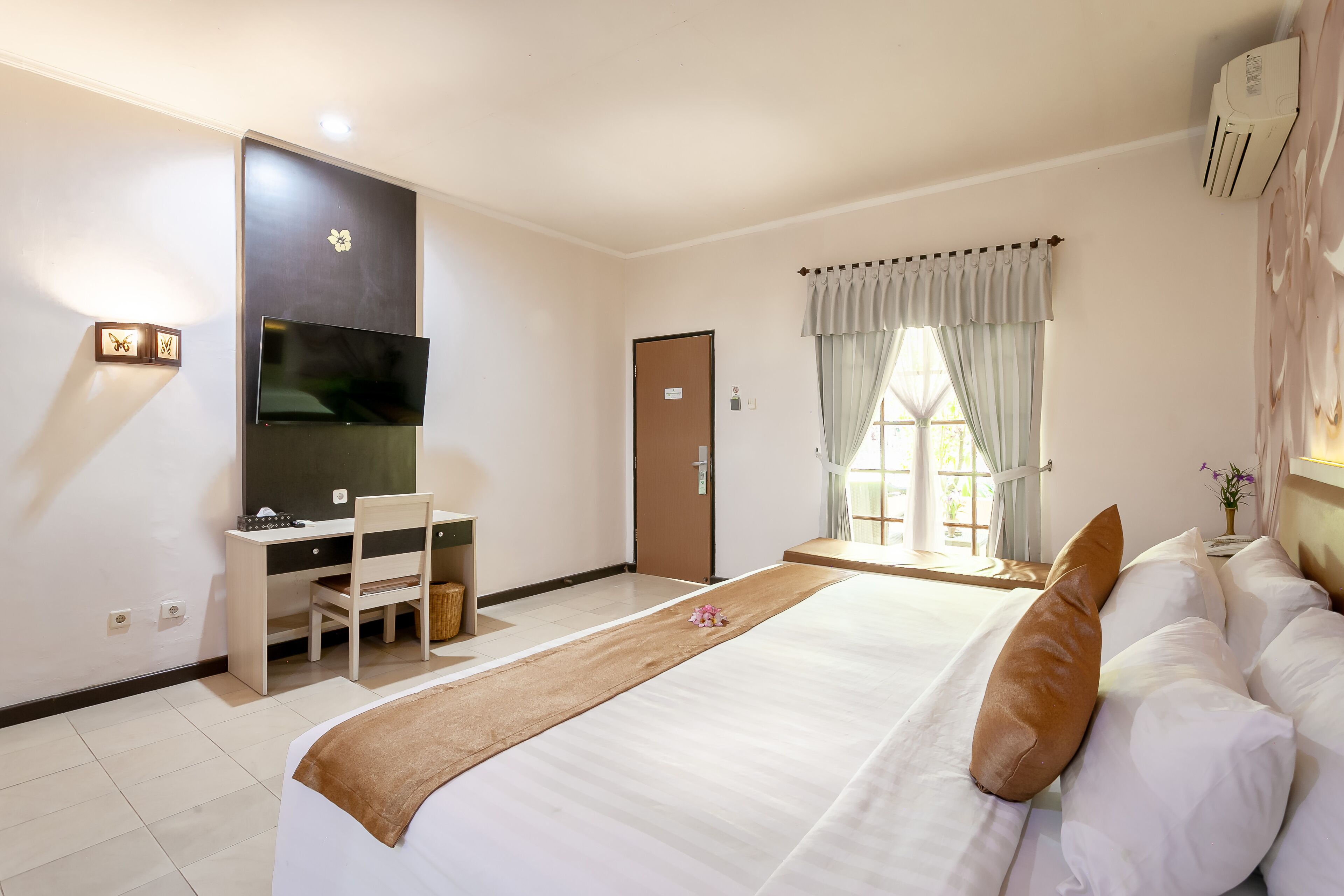 A bedroom with a bed, a desk, a chair, a television, a window with curtains, and an air conditioning unit.