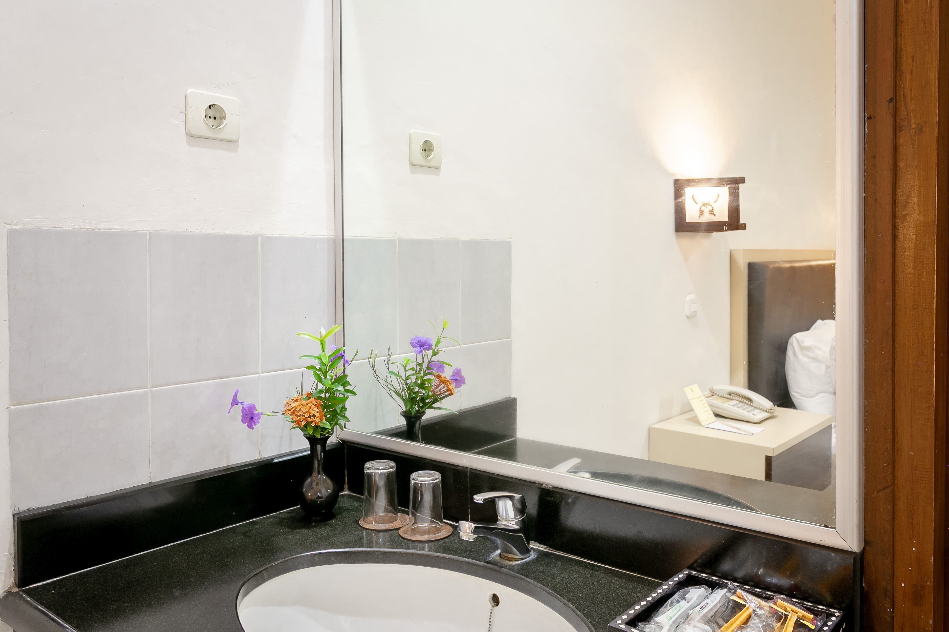 A bathroom with a large mirror, a sink, and a vase with flowers.
