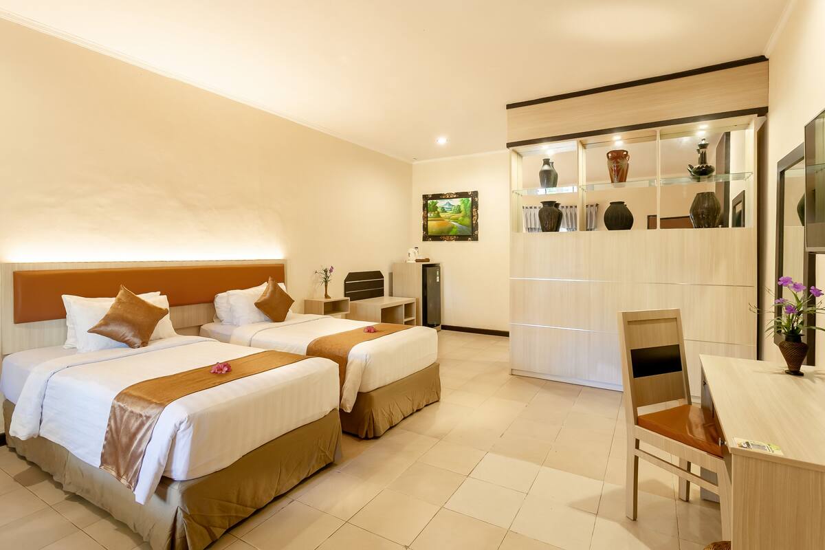 A hotel room with two beds, a desk, a chair, and a cabinet with decorative items.