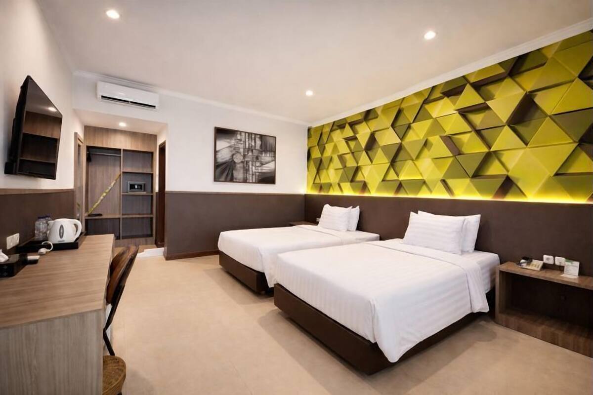 A hotel room with two beds, a desk, a chair, a microwave, and a wall with geometric patterns.
