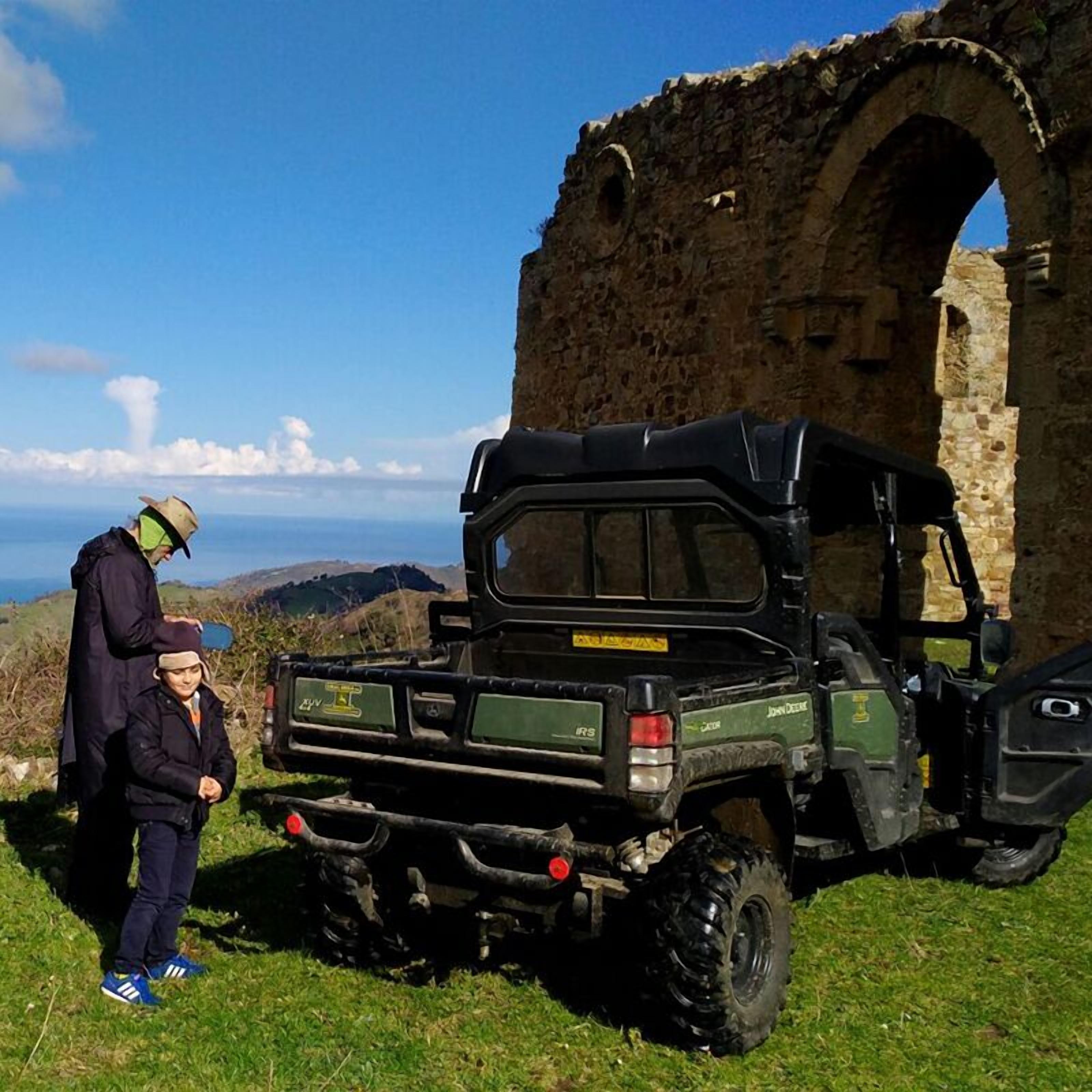 Un vehículo todoterreno robusto estacionado cerca de un arco de piedra, con una vista panorámica al fondo.