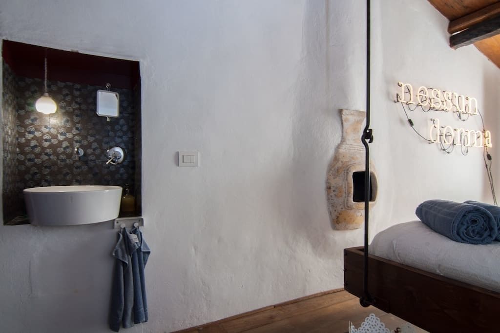 A bathroom with a round sink, hanging light, and a wall-mounted mirror.
