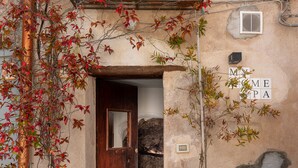 A rustic building with a wooden door, a balcony with potted plants, and a table with fruits. - Wundergarten Dimora dei Frati (Gratteri)