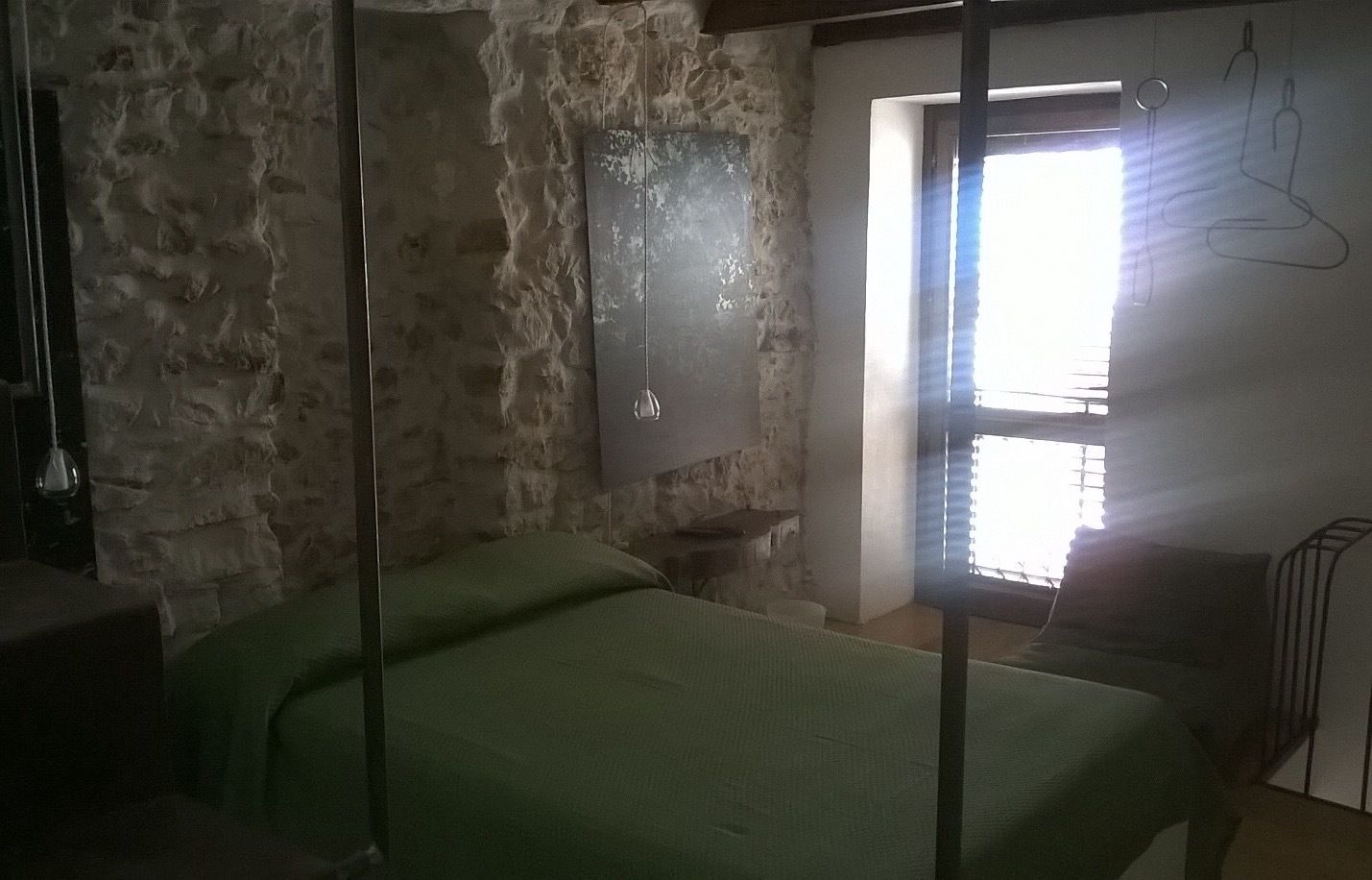 Ein Zimmer mit einer Steinstur, einem Bett mit grüner Bettwäsche, einer Hängeleuchte und einem Fenster mit Jalousien.