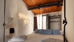 A bedroom with a wooden ceiling, a stone wall feature, a bed with white bedding, and a wall-mounted light fixture. - Wundergarten Dimora dei Frati (Gratteri)