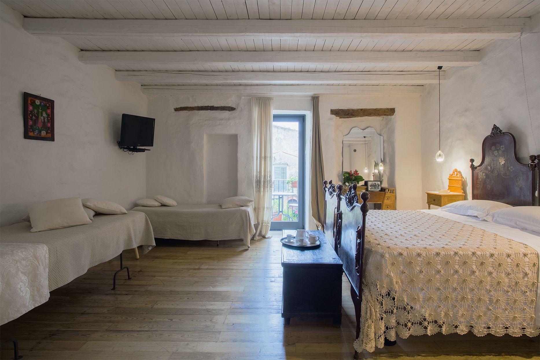 Un dormitorio con dos camas individuales, suelo de madera, televisor en la pared y ventana con cortinas.