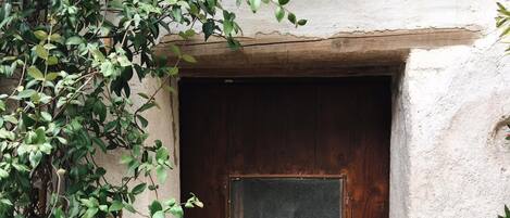 A wooden door with a small square window, set in a textured wall.