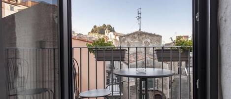 Un balcón con una mesa y dos sillas, con vistas a un paisaje urbano con edificios y una colina.