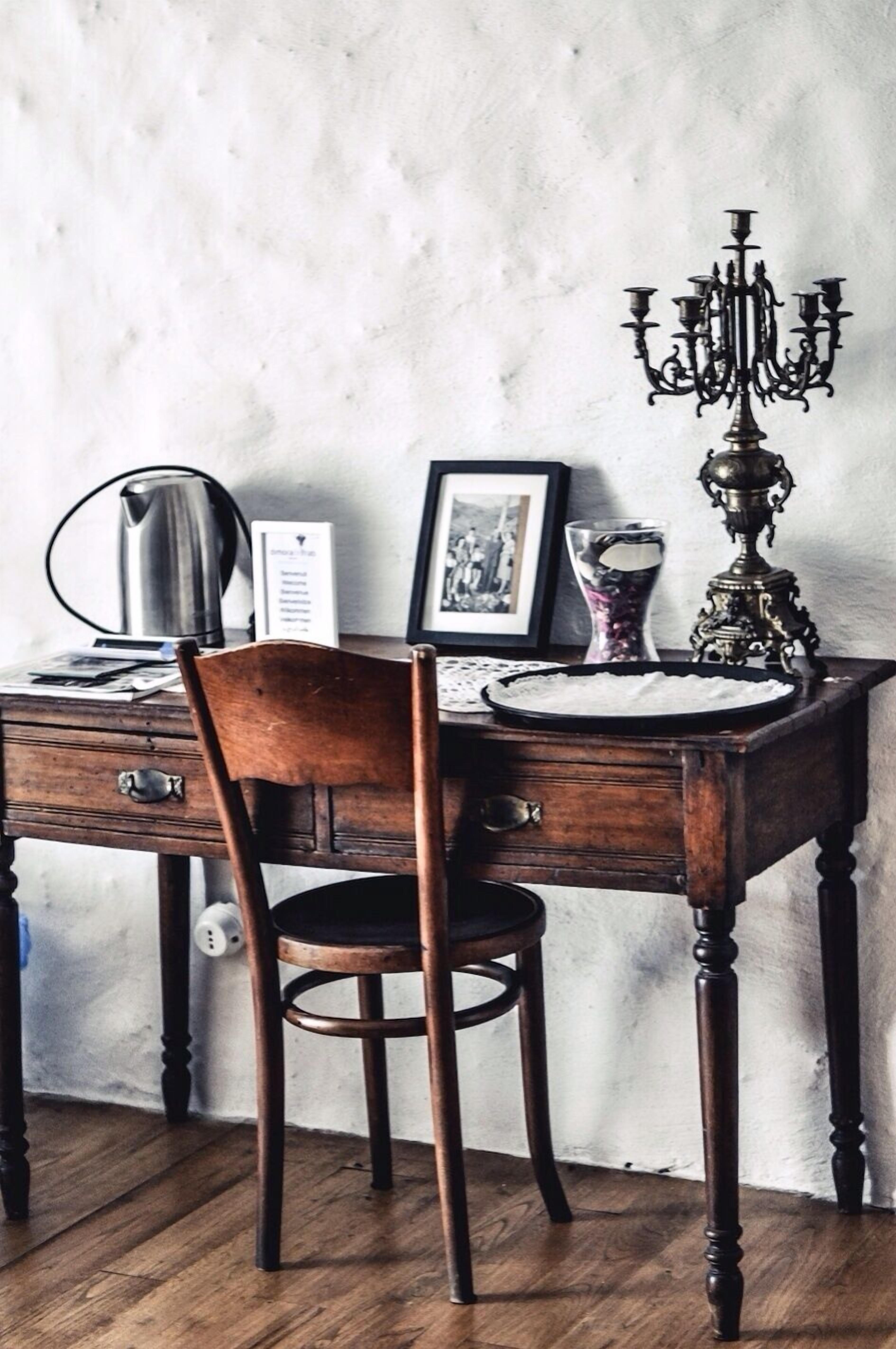 Una scrivania in legno con una sedia, un quadro incorniciato, un bollitore, un vaso di vetro e un candelabro.