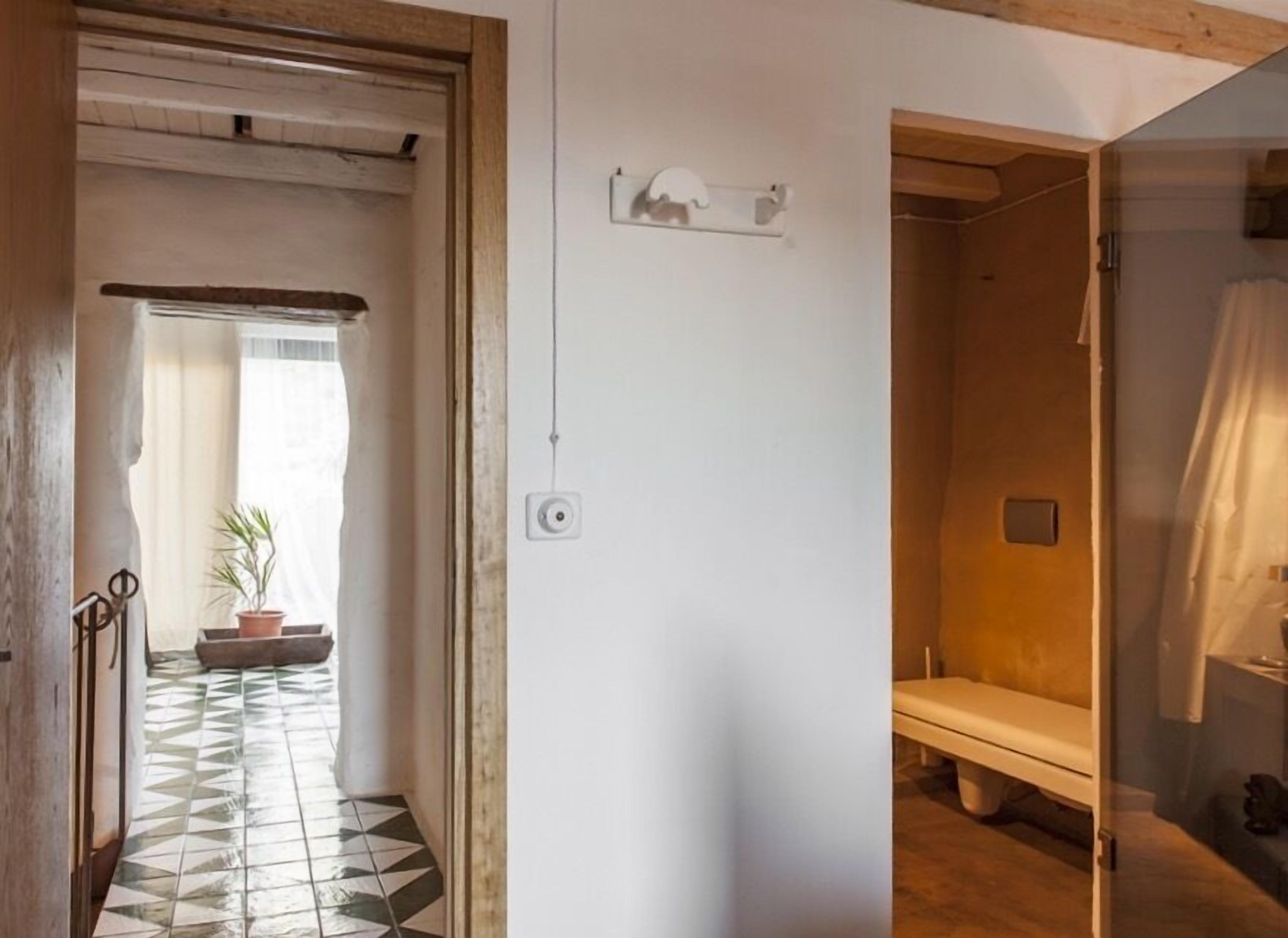 A room with a tiled floor, a bench, a small potted plant, and a white wall with a light switch and a small electrical outlet.