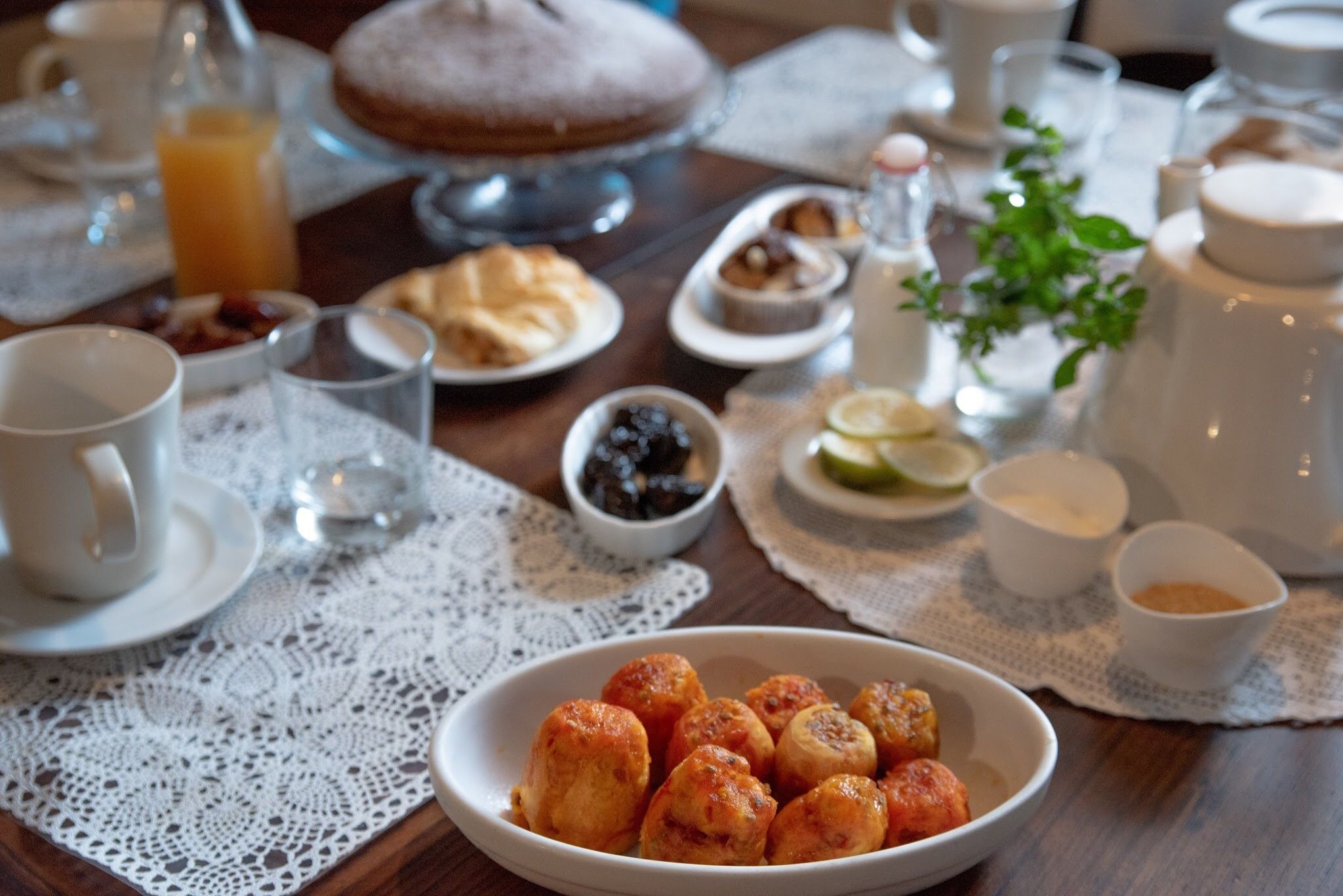 A breakfast table with various dishes, including a bowl of pastries, a cake, and a fruit bowl.