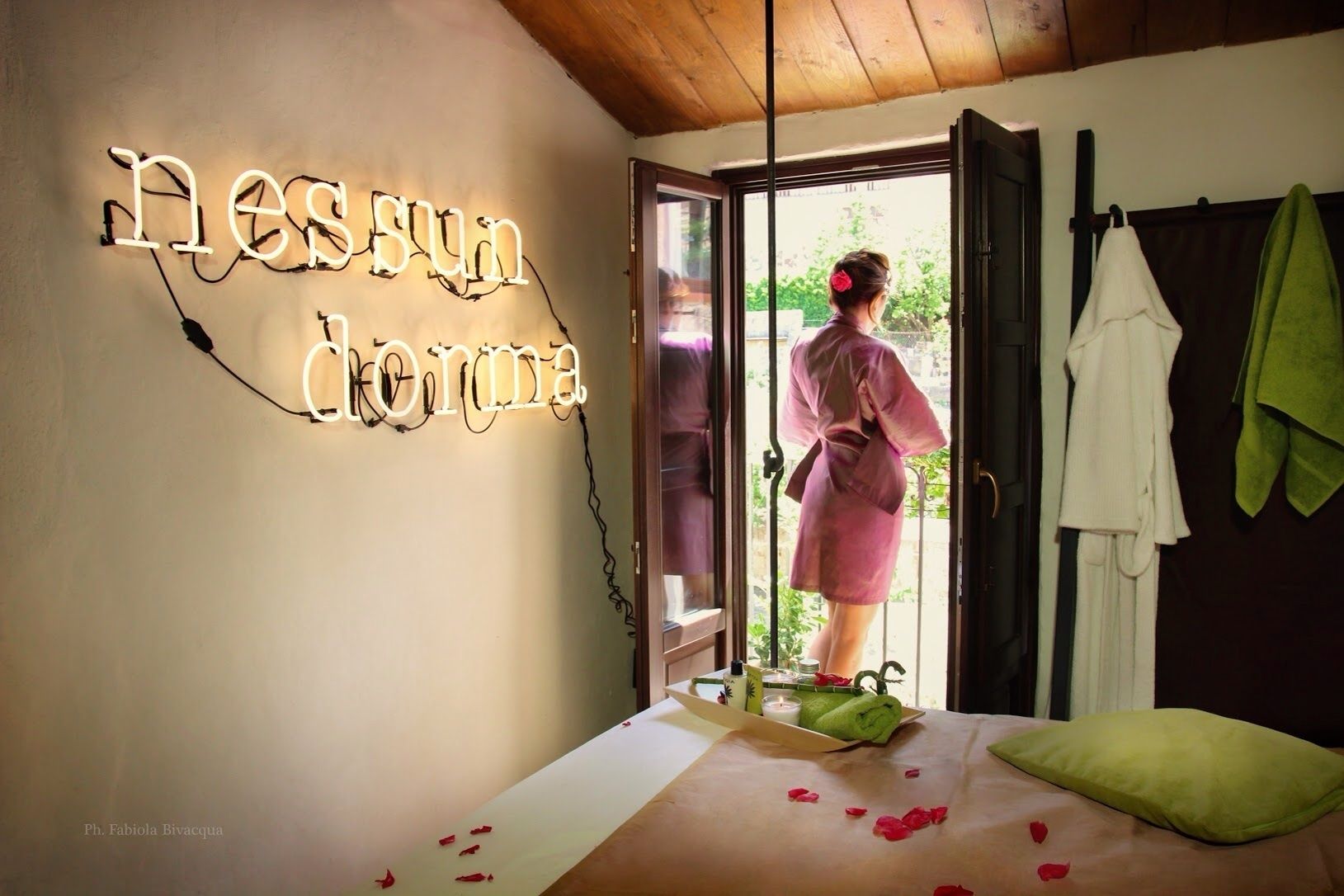 A room with a bed, a neon sign, and a view of the outdoors.