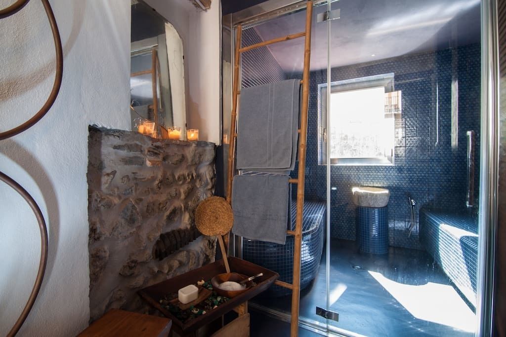 A bathroom with a stone wall, a wooden shelf with candles, a mirror, and a blue tiled floor.