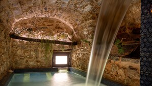 A stone-walled indoor pool with a waterfall feature, a bench, and a door leading outside. - Wundergarten Dimora dei Frati (Gratteri)