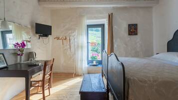 Un dormitorio con cama, escritorio con silla, televisión y ventana con vista a vegetación.
