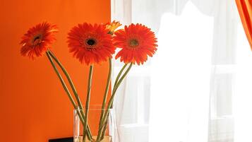 Un vaso di vetro trasparente con tre fiori arancioni su un tavolo tondo, di fronte a una parete arancione.